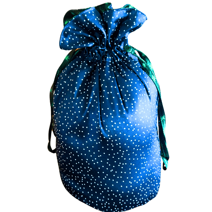 A blue reusable drawstring fabric gift bag pouch decorated with white polka dots and a green satin drawstring, isolated on a white background.