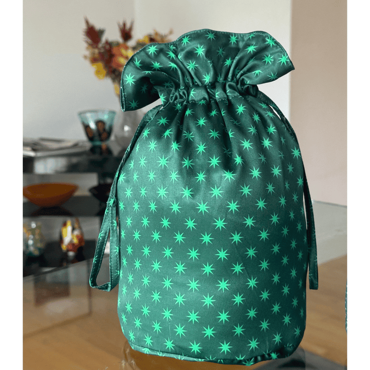 A green drawstring gift bag pouch with a repeating star pattern, shown standing on a glass table in an indoor setting.